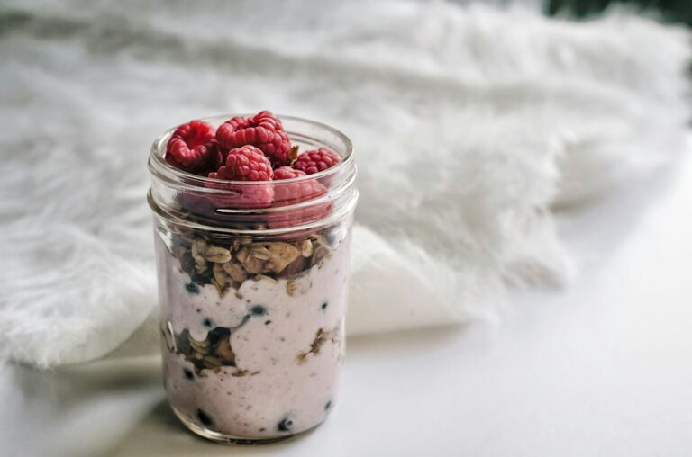 A glass jar filled with berries, yoghurt and oats.