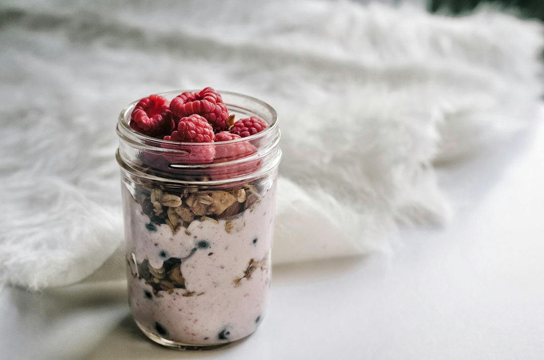 A glass jar filled with berries, yoghurt and oats.