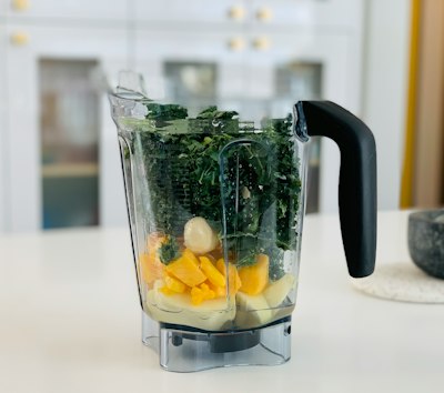 A blender jug filled with fruit and leafy greens.