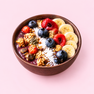 An açaí bowl topped with banana, strawberries, blueberries and granola on a soft pink background.