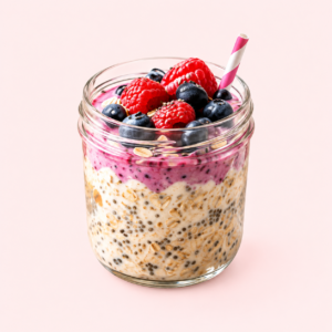 A glass jar of berry overnight oats with raspberries, blueberries and a striped straw on a pale pink background.